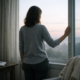 Woman standing by a window looking out at the landscape at dusk