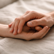 Close up of two people holding hands on a bed.